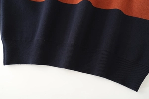 Detailed view of the orange and dark blue color block ribbed hem on a knit polo shirt