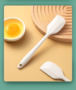 Close-up of white silicone spatula with wooden handle on a minimalist warm background