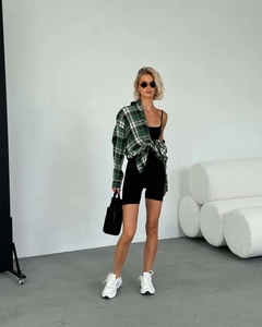 Street style shot of a loose green and black plaid shirt with black romper and sneakers