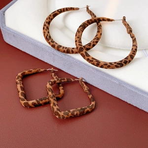 Détail de boucles d'oreilles léopard rondes et carrées sur fond de cuir texturé