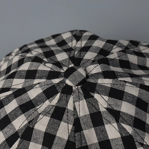 Close-up of linen newsboy cap featuring black and white checkered pattern and top button