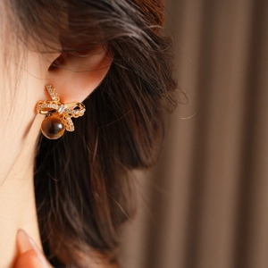 Close-up of golden bow earrings with zircon and tiger eye bead on a model ear