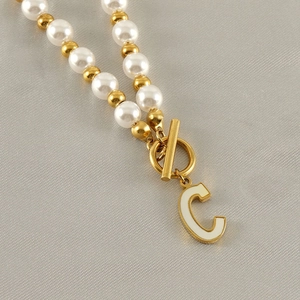 Macro detail of bead necklace with pearl, golden beads and white enamel letter C pendant