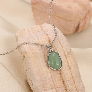 Close-up of green teardrop gemstone pendant on silver chain draped over natural stones