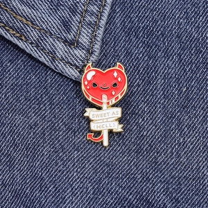 Detail of red heart devil lollipop enamel pin pinned on blue denim jacket fabric