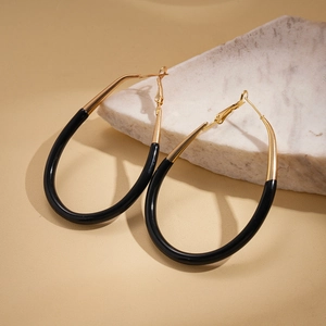 Macro detail of oval gold hoop earrings featuring bold black enamel contrast on marble base