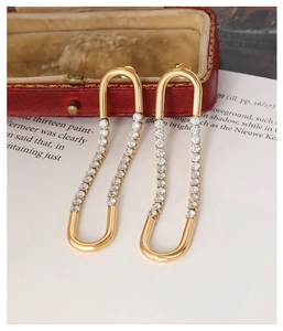 Detail of gold U-shaped earrings with zircon pavé accents on vintage book pages