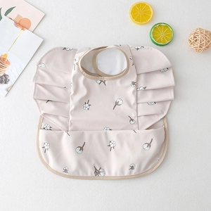 Detail of beige baby bib with cotton print and ruffles featuring a waterproof food catcher