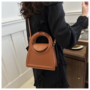 Brown trapezoid handbag with large circular handle and detachable shoulder strap on model