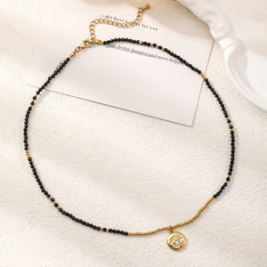 Detail of beaded necklace featuring black spinel, golden devil eye charm and lobster clasp
