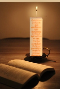 Pillar candle with scripture text on a metal base shown in a warm cozy setting