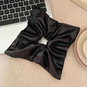 Large black pleated satin scrunchie hair tie on beige knit fabric background