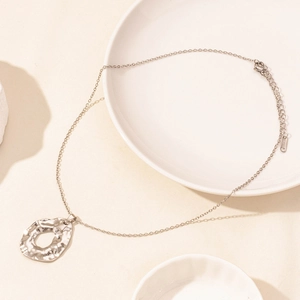 Macro detail of silver stainless steel necklace with lava texture pendant on ceramic dish