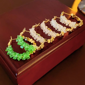 Détail de boucles d'oreilles créoles dorées en C avec pierres en cristal vert et blanc