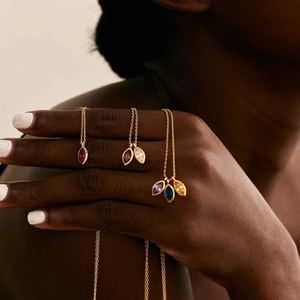 Three gold necklaces featuring marquise-cut birthstone pendants on a model's neck