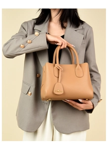 Close-up of light brown pebble leather handbag with gold hardware and charm detail