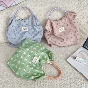 Tre borse shopper floreali in blu, rosa e verde con manici in corda su tappeto bianco
