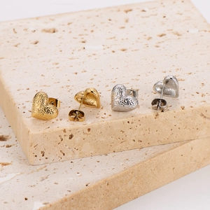 Detailed view of textured heart stud earrings in gold and silver finish on stone pedestals
