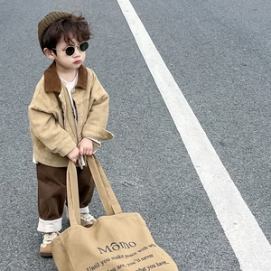 Detalle de niño con chaqueta de pana caqui y bolso tote de lona beige con letras