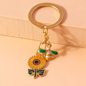 Macro shot of gold keychain with enamel sunflower and bee charms on beige background