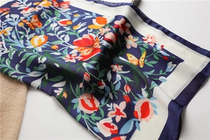 Detailopname van een zijden sjaal met bloemen- en vlinderprints op marineblauw en wit textiel