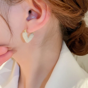 Detailed view of elegant gold heart earrings with white pearls on a female model