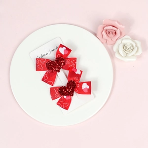 Detailed close-up of two red heart-patterned bow hair clips on a white display card