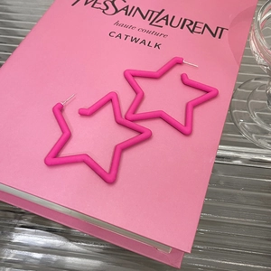 Detail of matte fuchsia star-shaped earrings on a fashion book background