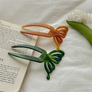 Elegant acetate butterfly hair fork in amber and dark green on an open book background