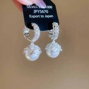 Detail of 925 silver hoop earrings with hollow patterns and large round white pearls