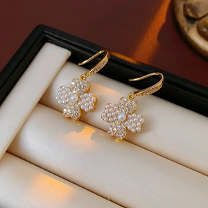 Close-up of gold-plated clover earrings with faux pearls and sparkling zircon stones