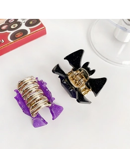 Detail of purple glitter fish hair clip and black glitter bat claw clip on white backdrop