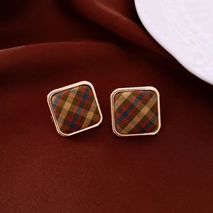 Détail macro de boucles d'oreilles carrées en tissu avec cadre doré et motif à carreaux