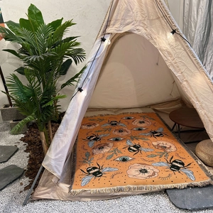 Detail of bohemian outdoor blanket with tassels, bees and eye patterns inside a tent
