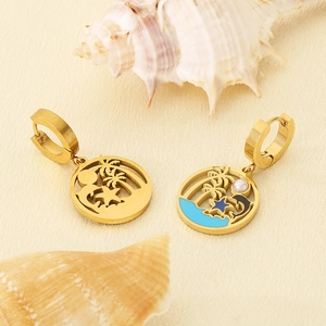 Detailed close-up of gold tropical dolphin earrings with blue enamel and pearl on a shell