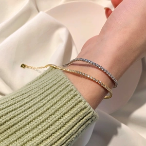 Close-up of gold and silver tennis bracelets with round zircons on a white fabric background