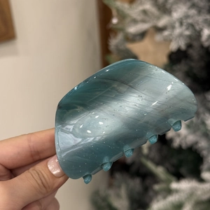 Detail of teal opal texture claw clip with glitter finish held against a festive tree