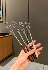 Detail of hand holding a stainless steel whisk with ergonomic wooden handle for baking