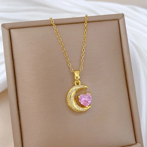 Detailed shot of moon-shaped gold necklace with pink heart stone and crystals in box