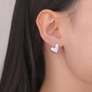 Polished silver heart stud earrings worn by a model showing size and texture