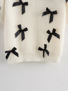 Detail eines weißen Strickpullovers mit schwarzen Bandschleifen und Rippbündchen