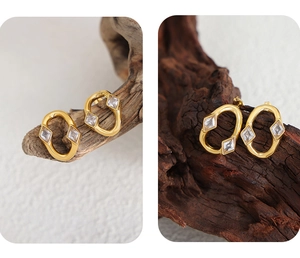 Close-up of golden oval stud earrings featuring sparkling square zircon stones on wood