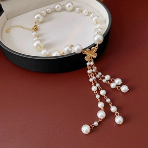 Detailed view of white pearl bracelet featuring a gold clover pendant and elegant tassels