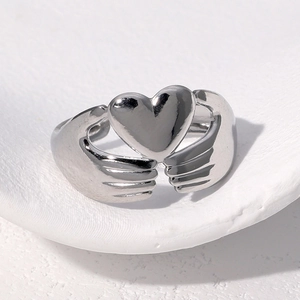 Macro shot of polished silver heart-shaped ring with unique double hand hug design