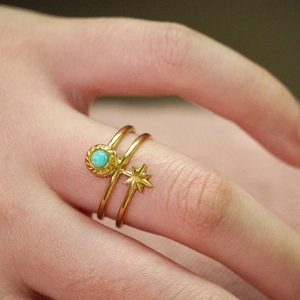 Bague en acier doré avec pendentif étoile et pierre turquoise sur le doigt d'un mannequin