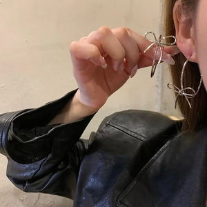 Detailed close-up of a silver bow knot hoop earring worn against a black leather jacket