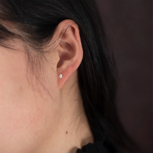 Close-up of minimalist gold flower stud earring with four zircon gemstones on ear