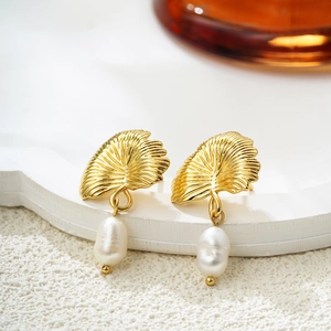Détail d'une boucle d'oreille feuille de ginkgo dorée avec perle d'eau douce
