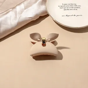 Detailed view of matte cream bow hair claw clip on elegant silk fabric background
