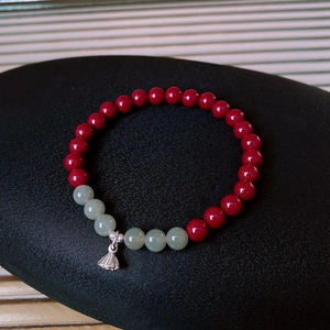 Macro detail of S925 silver lotus charm with cinnabar and jade beads on a beaded bracelet